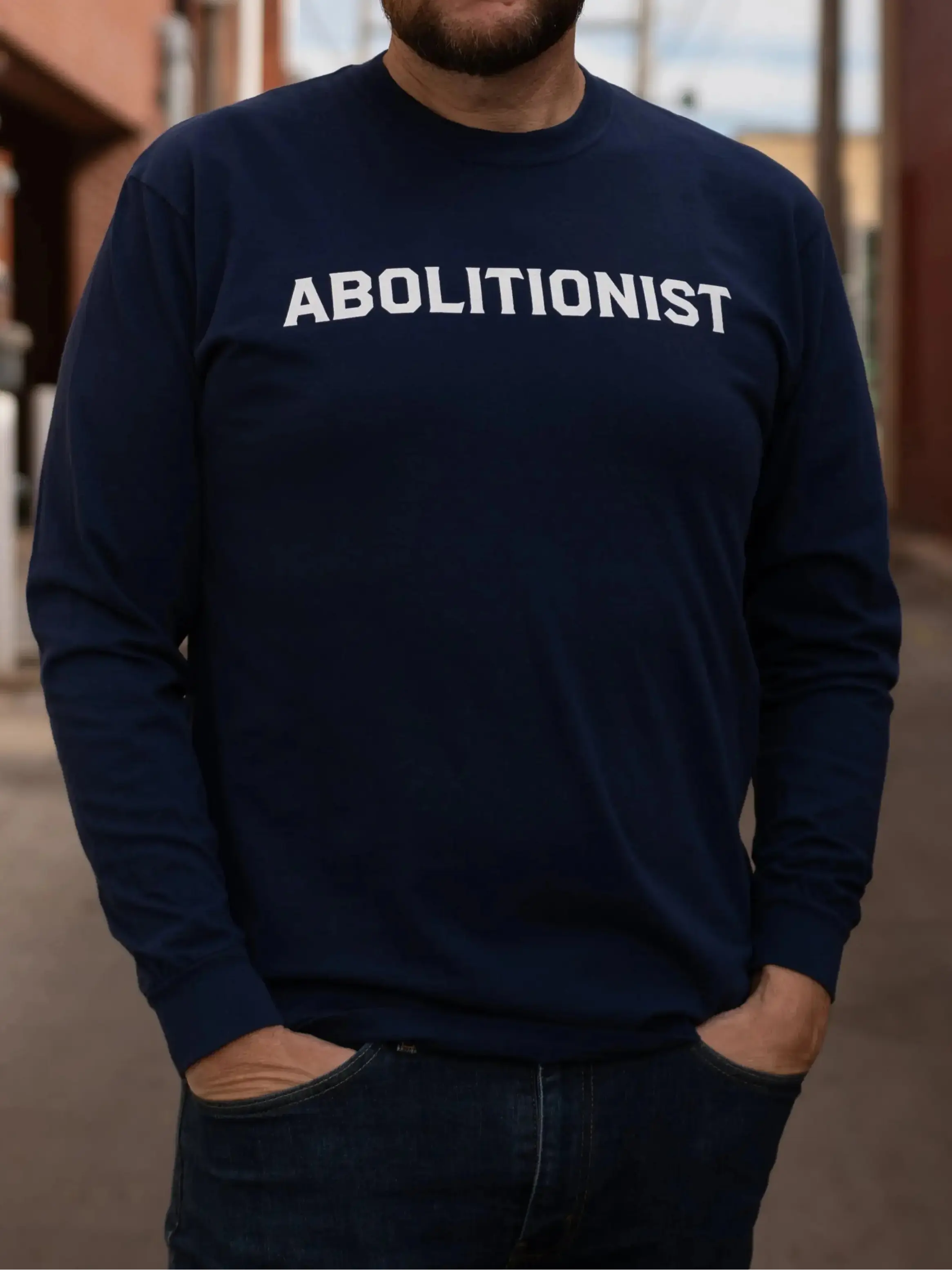 Man wearing a navy blue sweatshirt with 'ABOLITIONIST' text in an urban setting