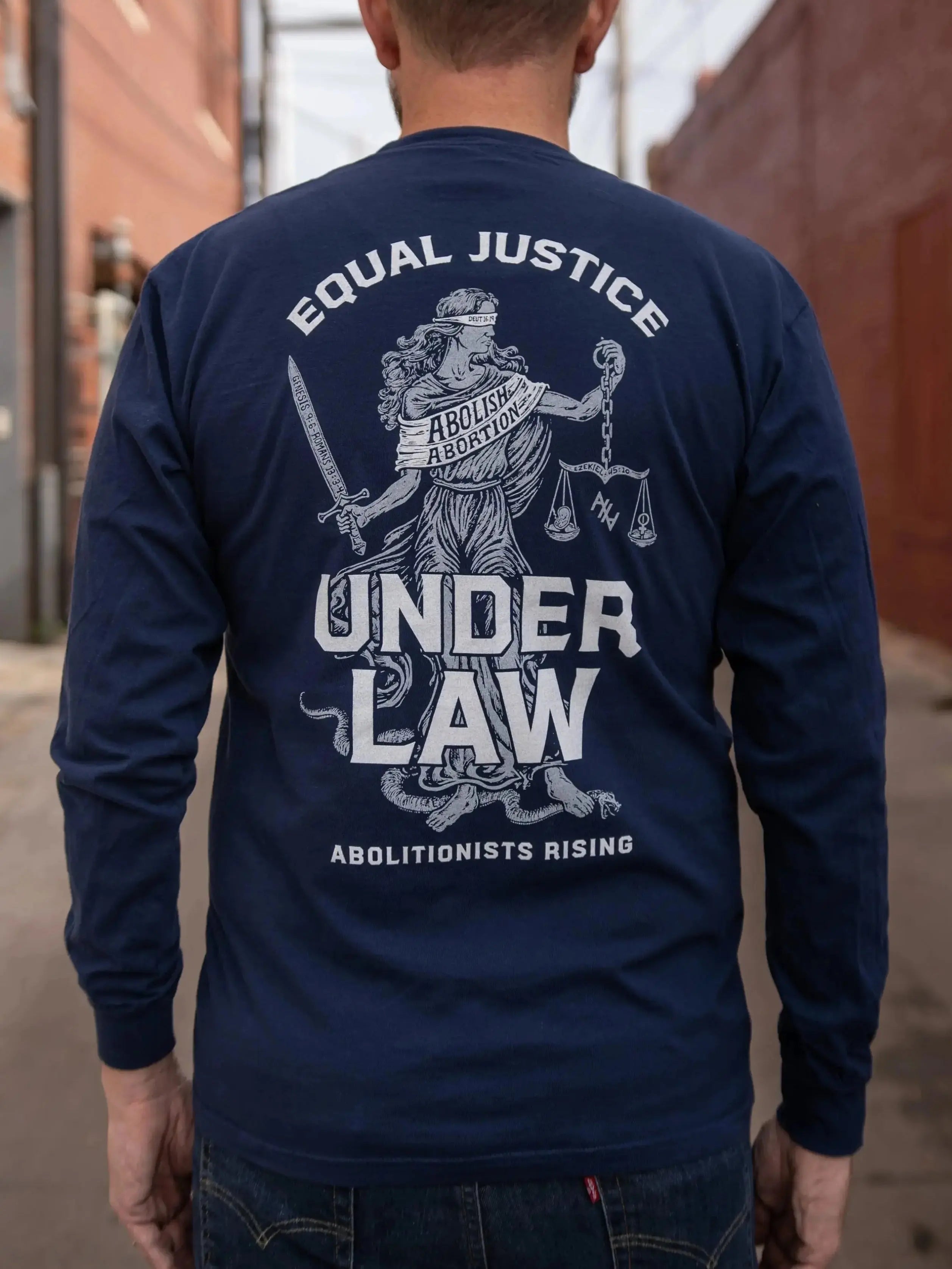 Person wearing a navy blue long-sleeve shirt with an Equal Justice Under Law graphic and text on the back, standing in an alleyway.