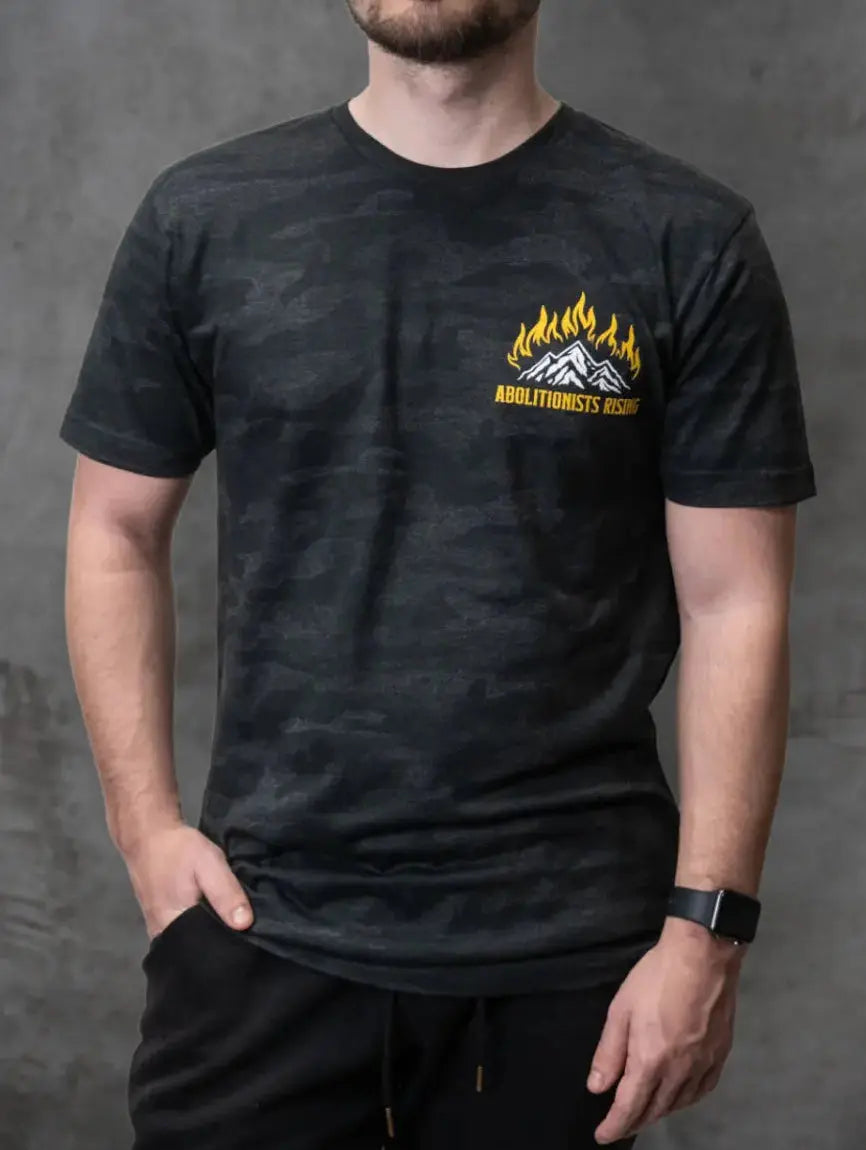 Man wearing a camo t-shirt with an Abolitionists Rising logo against a gray background
